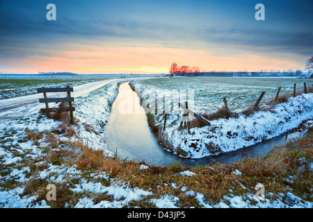 dramatic sunset over frozen river in Dutch farmland Stock Photo