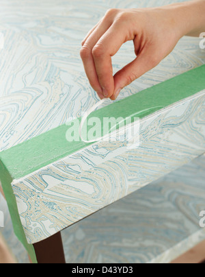 Close-up of Woman's Hand Applying Wallpaper to Table in Studio Stock Photo