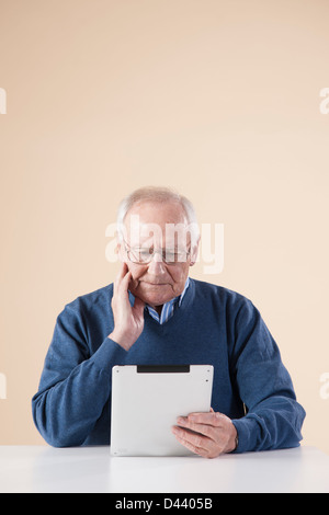 Senior Man Sitting at Table, Looking at Tablet PC, Studio Shot on Beige Background Stock Photo