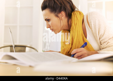 college student reading something in laptop screen and writing it down on her notes Stock Photo
