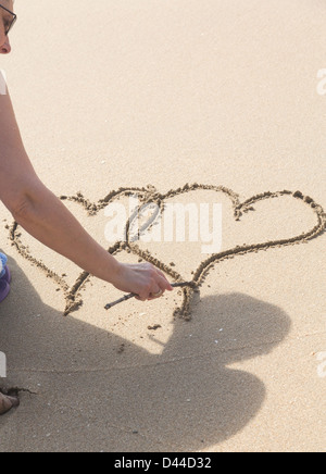 Lady drawing pair of linked hearts in sand on beach in Caribbean Stock Photo