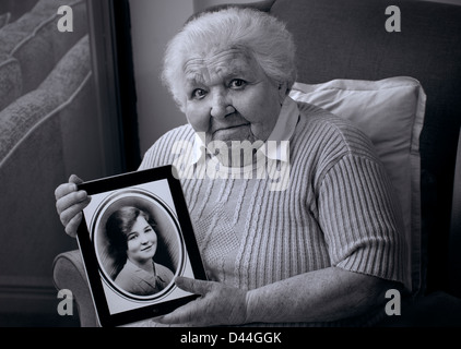 AGE AGEING GENES comparison 98 years old elderly lady holding iPad tablet computer, displaying sepia portrait of herself taken 80 years ago at age 18 Stock Photo
