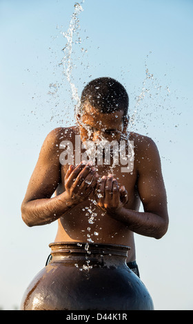 Indian man splashing water over himself from a water pot at sunset. India Stock Photo