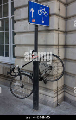 A bicycle has been locked high up on a City of London street sign post where arrows point up and down, the coincidence of a visual pun - in the heart of the capital's financial district. The authorities recommend locking up a bike in specified areas, making sure they're secured with a substantial D-lock. The bike is a Specialized road bike of a single-gear variety. Stock Photo