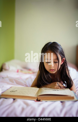 Girl lies in bed reading book