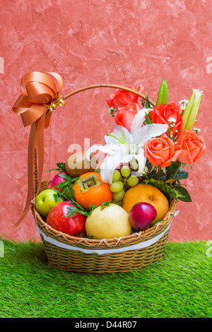 Basket of fruit and flower on green grass and grunge wall Stock Photo