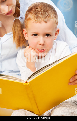 Five years old boy bored and prank with face expression while his mother trying to teach him to read Stock Photo