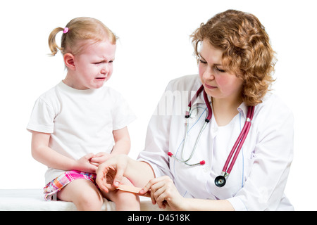 Crying child with scratched knee. Doctor provides first aid. Stock Photo