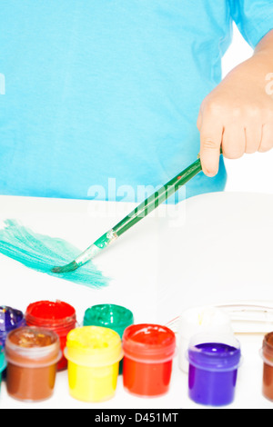 Close-up of paints with small kid's hand holding paintbrush and drawing on paper Stock Photo