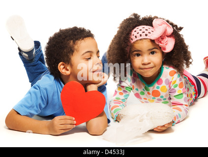 Black boy laying on the floor with little girl with frizzy hair holding red heart made of paper Stock Photo