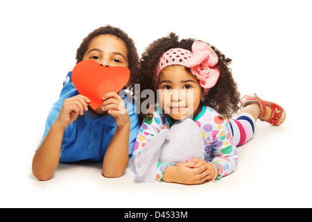 Black boy laying with little girl with frizzy hair holding red heart made of paper Stock Photo