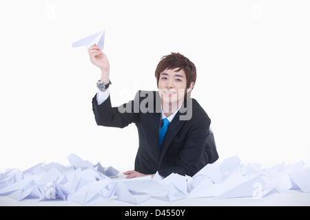 a businessman holding a paper planes while lying on the floor full of paper planes Stock Photo