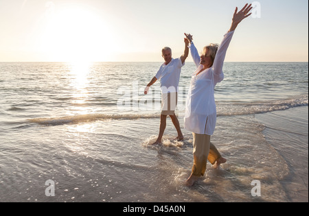 Happy senior man and woman couple dancing and holding hands on a deserted tropical beach at sunrise or sunset Stock Photo