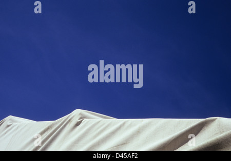 Detail of large item covered with white plastic tarpaulin sheet under deep blue sky Stock Photo