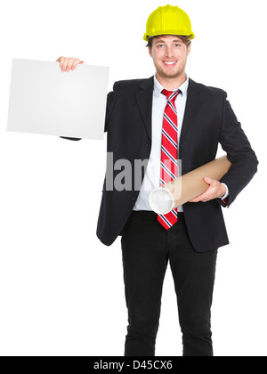 Young happy smiling Caucasian male engineer / architect showing blank sign holding plans and wearing yellow helmet Stock Photo