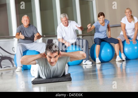 Man doing back exercises in gym with senior people around him Stock Photo