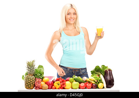 Beautiful young female holding a glass of juice behind a table full of fruits and vegetables isolated on white background Stock Photo