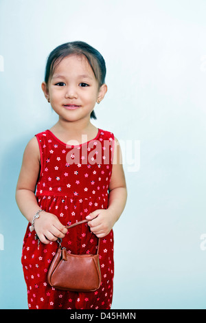 an asian gril wearing a read velvet dress and carrying a purse against a pale blue background Stock Photo