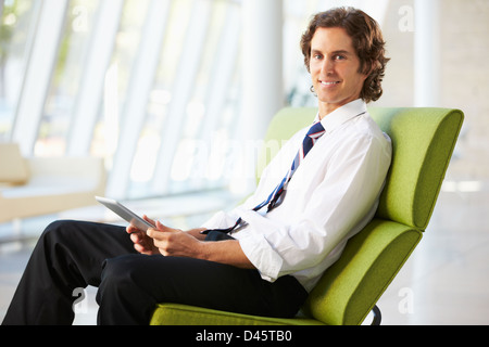 Businessman Sitting On Sofa In Office Using Digital Tablet Stock Photo