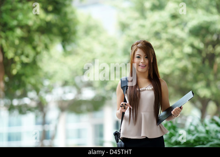 Young woman in business attire, carrying briefcase and holding folder standing outside. Stock Photo