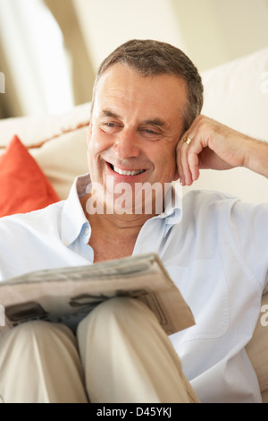 Senior Man Relaxing On Sofa At Home Reading Newspaper Stock Photo