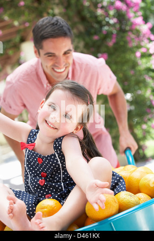 Man Pushing Woman In Wheelbarrow Filled With Oranges Stock Photo