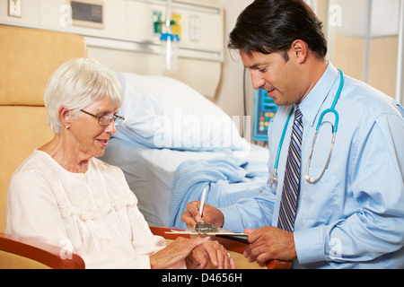 Doctor Taking Notes From Senior Female Patient Seated In Chair By Hospital Bed Stock Photo
