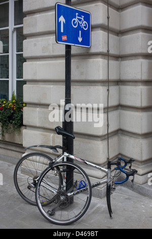 A bicycle has been dismantled, its front wheel detached from the frame on a City of London street sign post where arrows point up and down, the coincidence of a visual pun - in the heart of the capital's financial district. The authorities recommend locking up a bike in specified areas, making sure they're secured with a substantial D-lock. The bike is a Canondale road bike of a single-gear variety. Stock Photo
