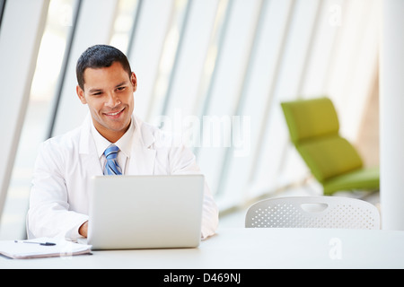 Doctor Using Laptop Sitting At Desk In Modern Hospital Stock Photo