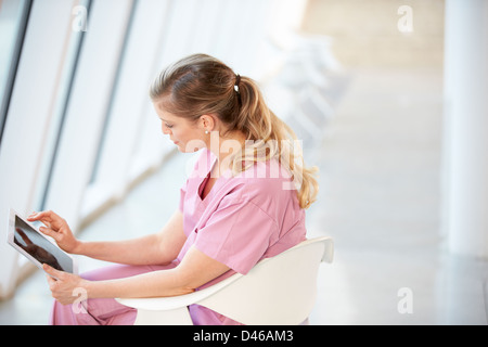 Female Nurse Sitting In Chair Using Digital Tablet Stock Photo