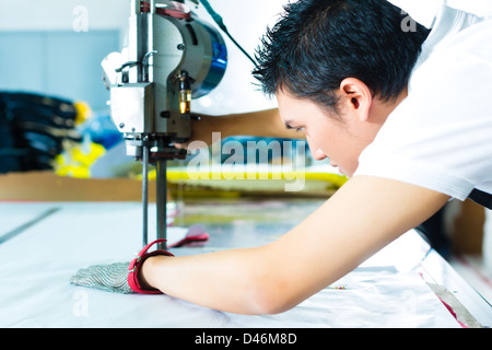 worker using a cutter - a large machine for cutting fabrics- in a Chinese textile factory, he wears a chain glove Stock Photo