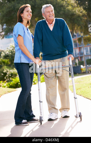 Carer Helping Senior Man With Walking Frame Stock Photo