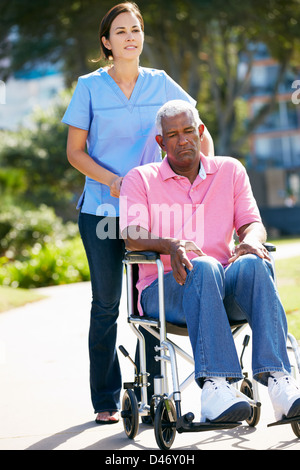 Carer Pushing Unhappy Senior Man In Wheelchair Stock Photo