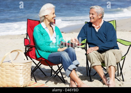 Senior Couple Sitting On Beach In Deckchairs Having Picnic Stock Photo