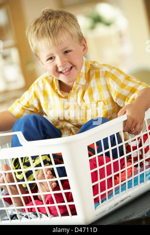 Boy Sitting In Basket Sorting Laundry On Kitchen Counter Stock Photo