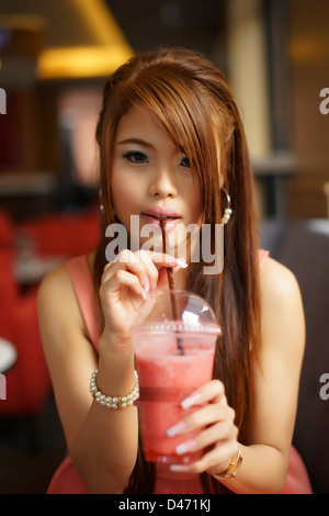 Young beautiful woman sitting in cafe holding and drinking a fruit smoothie through a straw. Stock Photo