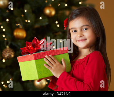 Girl Holding Christmas Present In Front Of Tree Stock Photo