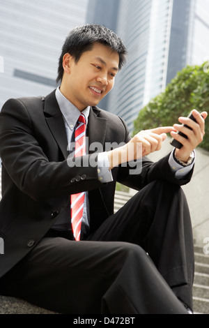 Chinese Businessman Dialling On Mobile Phone Outside Office Stock Photo