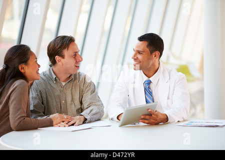 Doctor Using Tablet Computer Discussing Treatment With Patients Stock Photo