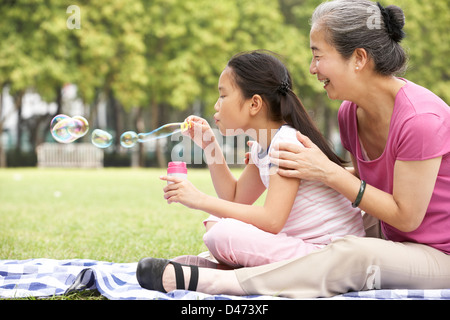 Chinese Grandmother With Granddaughter In Park Blowing Bubbles Stock Photo