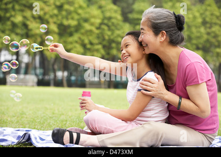 Chinese Grandmother With Granddaughter In Park Blowing Bubbles Stock Photo