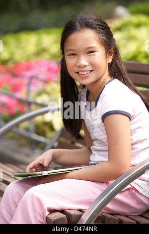 Portrait Of Chinese Girl Sitting On Park Bench With Digital Tablet Stock Photo