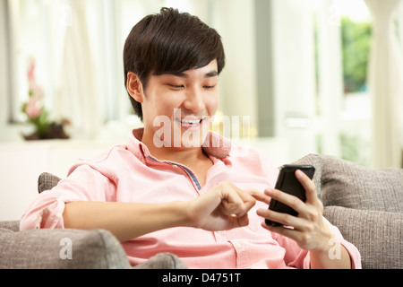 Young Chinese Man Using Mobile Phone On Sofa At Home Stock Photo