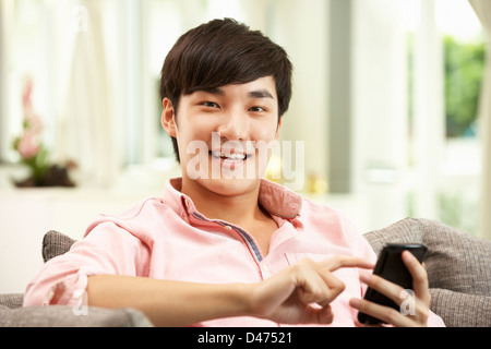 Young Chinese Man Using Mobile Phone On Sofa At Home Stock Photo