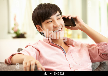 Young Chinese Man Using Mobile Phone On Sofa At Home Stock Photo
