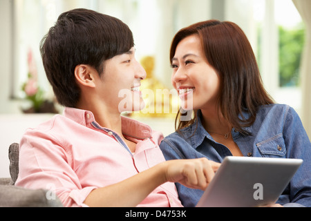 Young Chinese Couple Using Digital Tablet Whilst Relaxing On Sofa At Home Stock Photo