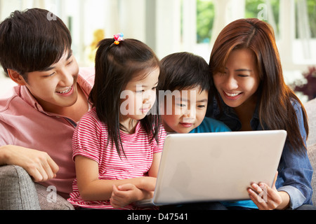 Chinese Family Using Laptop Whilst Relaxing On Sofa At Home Stock Photo