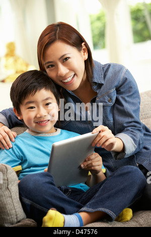 Chinese Mother And Son Using Tablet Computer Whilst Sitting On Sofa At Home Stock Photo