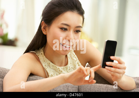 Young Chinese Woman Using Mobile Phone On Sofa At Home Stock Photo