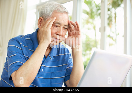 Worried Senior Chinese Man Sitting At Desk Using Laptop At Home Stock Photo